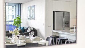 Una cocina moderna con electrodomésticos de acero inoxidable, un comedor con una mesa blanca para cuatro personas y una sala de estar con un sofá y una planta en maceta.