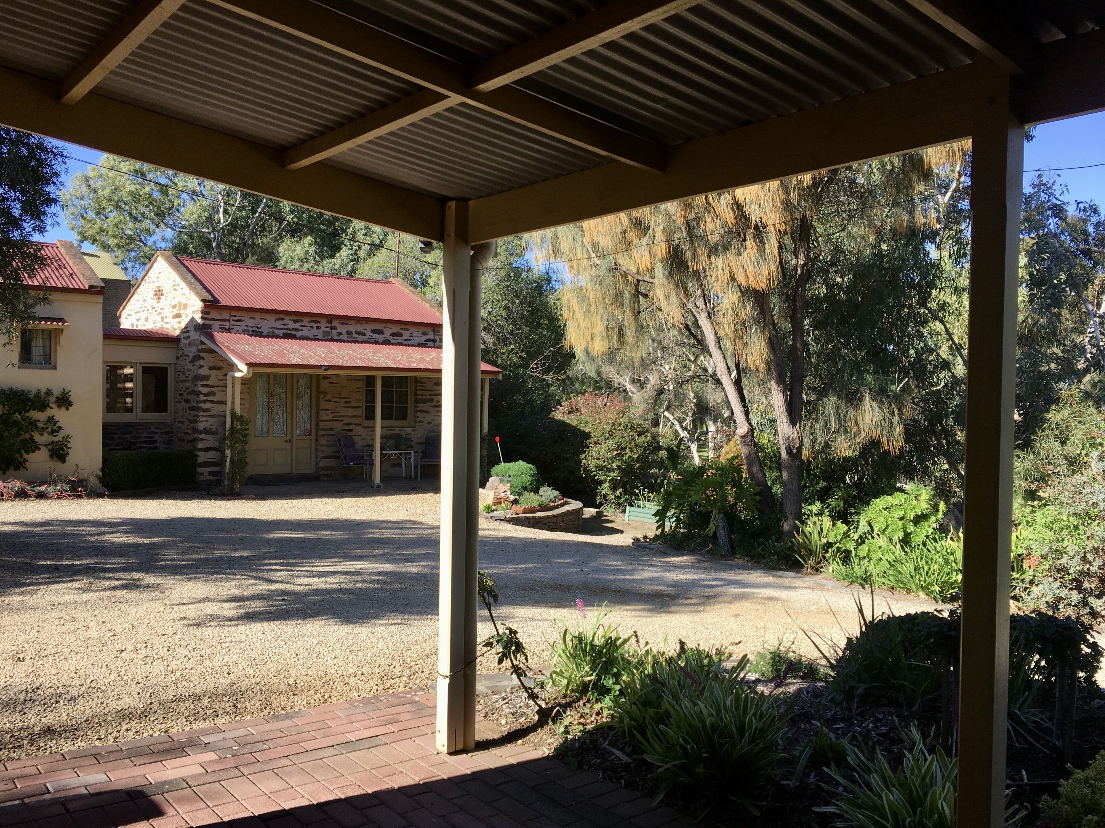 A covered outdoor area with a stone building in the background, surrounded by greenery and trees.