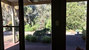 A view through a glass door into a garden area with a brick pathway, surrounded by various plants and trees. - Ideal location to explore historic Strathalbyn, Wineries, good food and scenery (Strathalbyn)