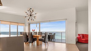 A modern living room with a dining area, large windows with ocean views, and a red chair. - Tranquility Bay of Fires - A beautiful beach house in a stunning location (The Gardens)