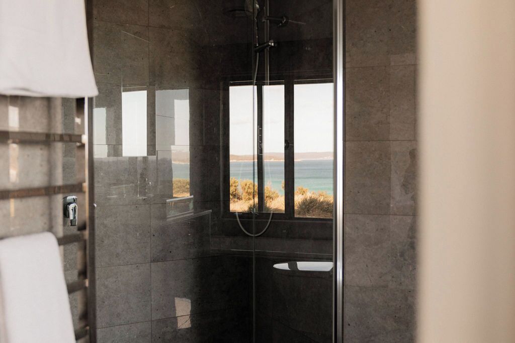 Un baño moderno con cabina de ducha de vidrio, vistas a la playa y un perchero para toallas.