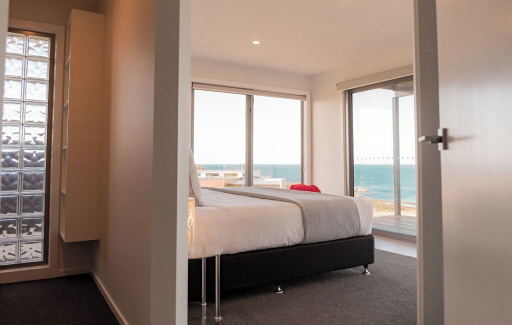 Un dormitorio con cama, vista al mar y puerta que da a un balcón.