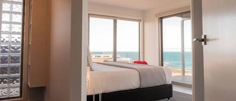 Un dormitorio con cama, vista al mar y puerta que da a un balcón.