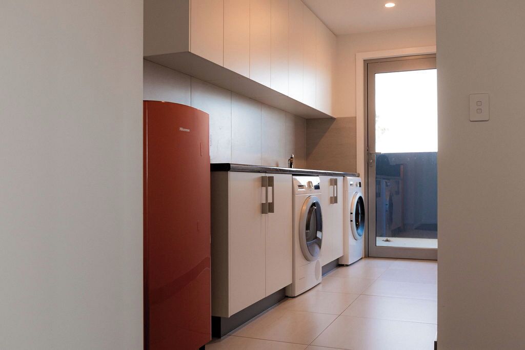 A modern laundry room with a red appliance, two washing machines, and a large window.