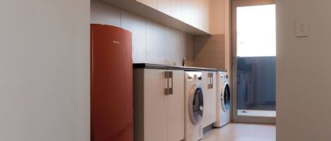 A modern laundry room with a red appliance, two washing machines, and a large window.