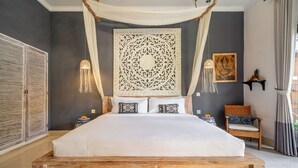 Ein Schlafzimmer mit einem hölzernen Bett, einem dekorativen Kopfteil, Nachttischen mit Lampen und einem Sessel.