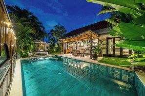 A swimming pool with a covered patio area, surrounded by lush greenery and a modern house with large windows. - Villa Sarong 2 Chic 2BR Boho Villa: Prime Central Location (Seminyak)