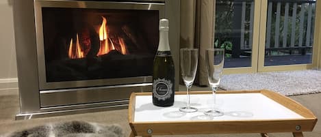 A fireplace with a bottle of champagne and two glasses on a small wooden table.