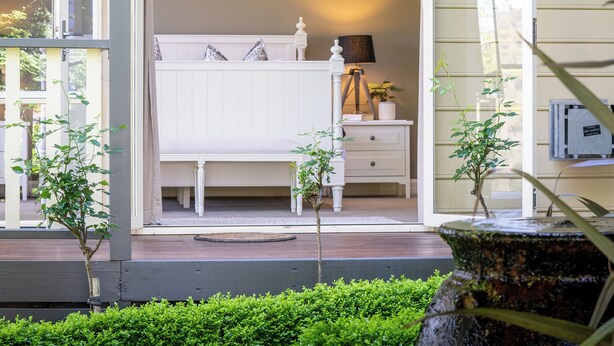 A bedroom with a white bed, a bedside table, and a lamp. There is a window with curtains, and a small plant on the bedside table. - Private Suite, Spa, Double shower, log fire, rural views & farm animals (Emerald)