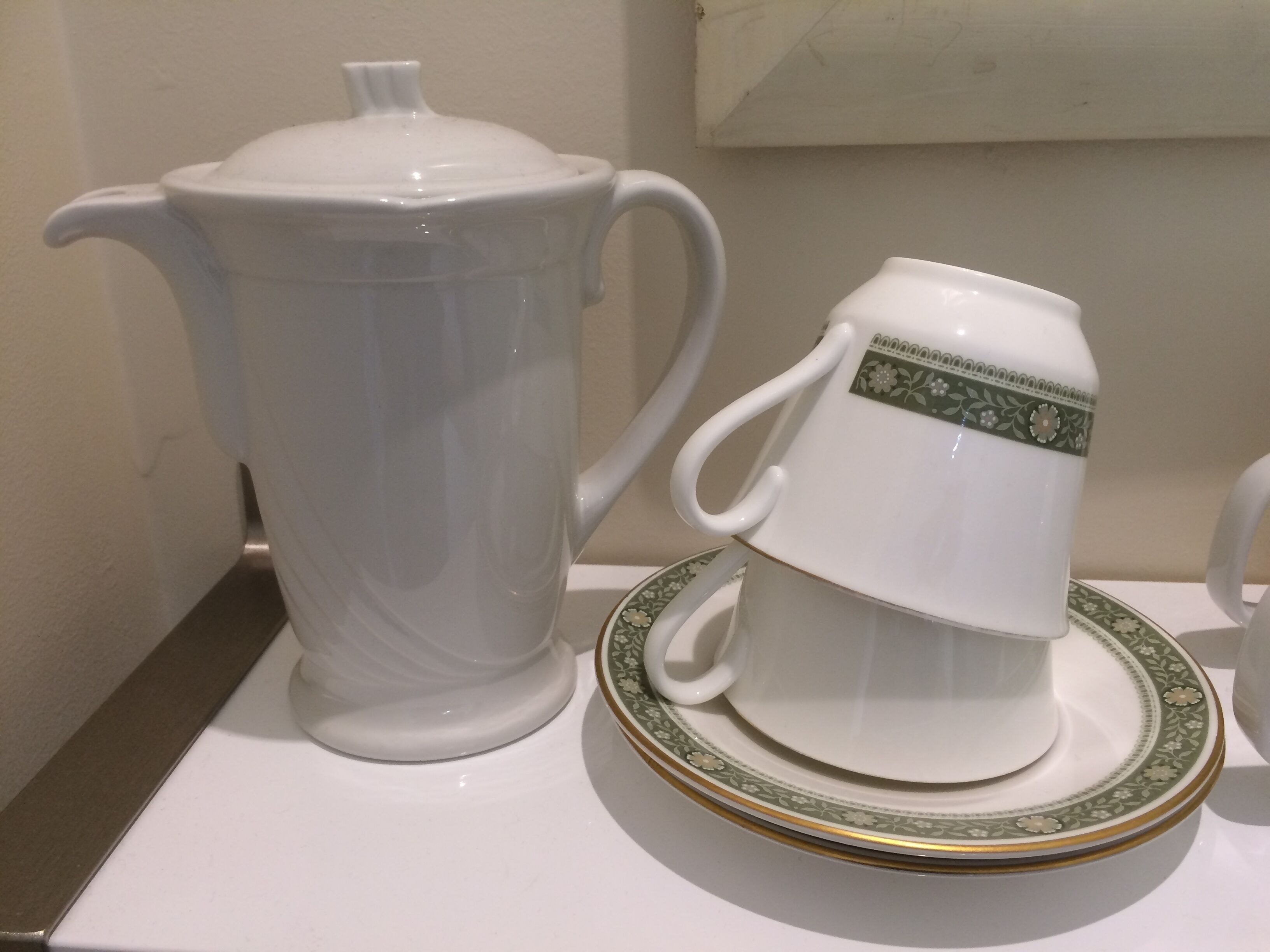 A white teapot and a matching cup and saucer on a white table.