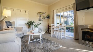 A living room with a fireplace, a sofa, a coffee table, and a TV. - Private Suite, Spa, Double shower, log fire, rural views & farm animals (Emerald)