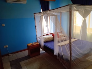 Relax in a cozy room with a single bed, canopy bedspread, and mosquito net, featuring a tiled floor and a window with curtains.