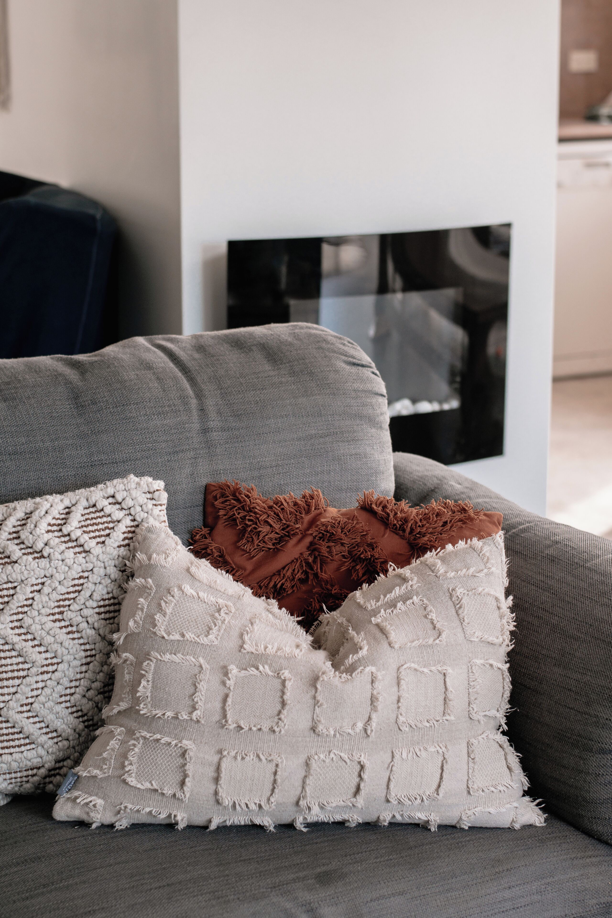 A grey sofa with three decorative pillows, a woven throw, and a black framed artwork on the wall.