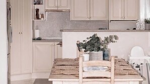 Uma cozinha com armários claros, uma mesa de madeira com um banco e um lustre.