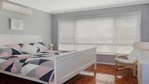 Una camera da letto con un letto, una sedia, una finestra con persiane, un termosifone e un quadro appeso al muro.