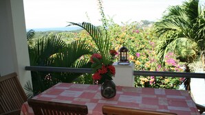A balcony with a table and chairs, overlooking a lush garden and a view of the ocean. - Villas Casa Loma - Suite 203 : Tropical Villa with Pool and Spectacular Views (Playa Flamingo)