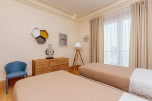 Two beds with matching linens, a dresser, and a chair create a comfortable retreat.