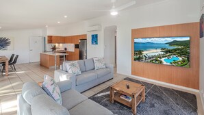 Een moderne woonkamer met een grijze bank, een salontafel en een televisie waarop een uitzicht op het strand te zien is.