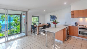 Een moderne keuken met een eethoek, grote ramen en uitzicht op groen.