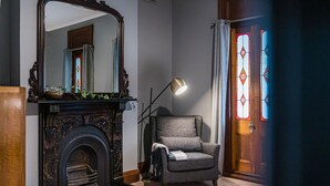 Une pièce avec une cheminée, un fauteuil, une lampe et une porte ornée de vitraux.