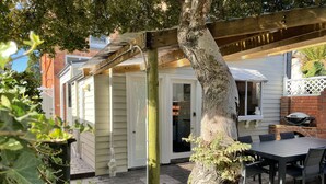 Une terrasse couverte avec une table et des chaises, un barbecue en briques et une porte blanche.
