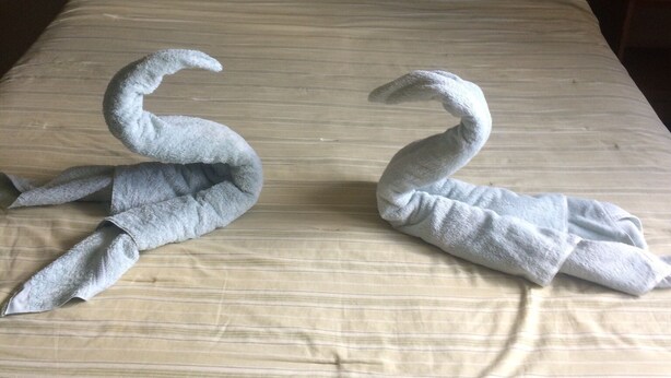 A bed with a striped bedspread and two towels shaped like swans.