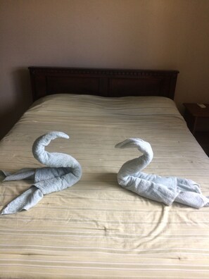 A bed with a striped bedspread and two towels shaped like swans.