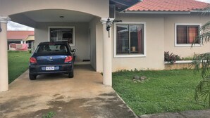 A house with a covered driveway, a parked car, and a garden with rocks and plants.