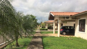 A pathway leading to a building with a tiled roof, a parked car, and lush greenery.