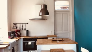 A kitchen with a wooden countertop, a hanging pendant light, a stove, and a window with a view.