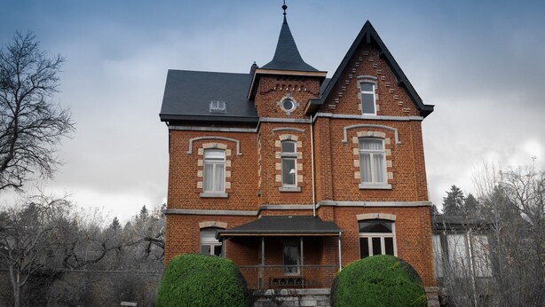 A large, two-story brick building with a steeply pitched roof, a prominent tower, and symmetrical windows.