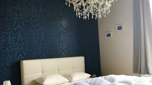A bedroom with a large bed, a nightstand, a white lamp, and a chandelier.