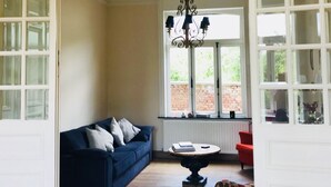 A spacious room with a blue sofa, a round table, and a red chair. There is a large window with a view of greenery outside.