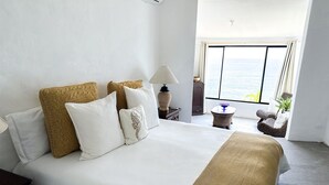 A hotel room with a large bed, a view of the sea, a small round table, and a chair. - AMAZING BEACH HOUSE ON A CLIFF, Spectacular OCEAN VIEWS & private beach access  (El Sunzal)