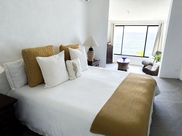 Une chambre d’hôtel avec un grand lit, une vue sur la mer, une petite table ronde et une chaise.