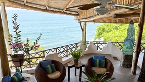 A covered outdoor seating area with a view of the sea, featuring wicker furniture and a round table with a plant. - AMAZING BEACH HOUSE ON A CLIFF, Spectacular OCEAN VIEWS & private beach access  (El Sunzal)