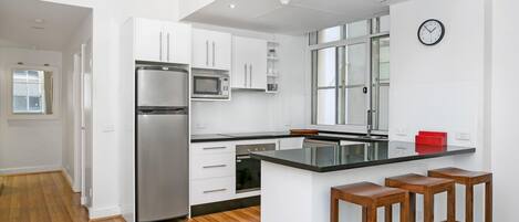 A modern kitchen with white cabinetry, stainless steel appliances, a black countertop island, and wooden stools.