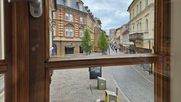 A street view through a window with brick buildings, a cobblestone street, and a few pedestrians. - Jager 2 Tour As / 1-room APP with AC, Wi-Fi, in the pedestrian zone (Ljubljana)