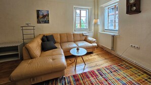 A living room with a leather sofa, a small round table, a colorful rug, a lamp, a clock, and a radiator. - Jager 2 Tour As / 1-room APP with AC, Wi-Fi, in the pedestrian zone (Ljubljana)