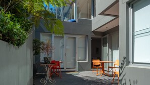 A modern outdoor seating area with a table and chairs, a potted plant, and a glass door leading to a building. - Quiet Relaxation Retreat Near Bondi Beach, The Cute Place To Put Up Your Feet (North Bondi)