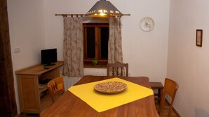 A dining area with a wooden table, chairs, a yellow placemat, a woven basket, a clock on the wall, and a window with curtains. - Waterwheel apartment at Kamenný potok (Kájov)