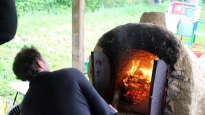 A person using a large, traditional oven with a fire inside, likely for cooking or baking. - Waterwheel apartment at Kamenný potok (Kájov)