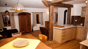 A cozy kitchen with wooden cabinets, a dining table with a placemat, and a hanging light fixture. - Waterwheel apartment at Kamenný potok (Kájov)