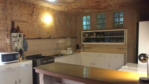 Et køkken med hvide skabe, en mikrobølgeovn, en komfur og en vask. To barstole og en hylde med glas.