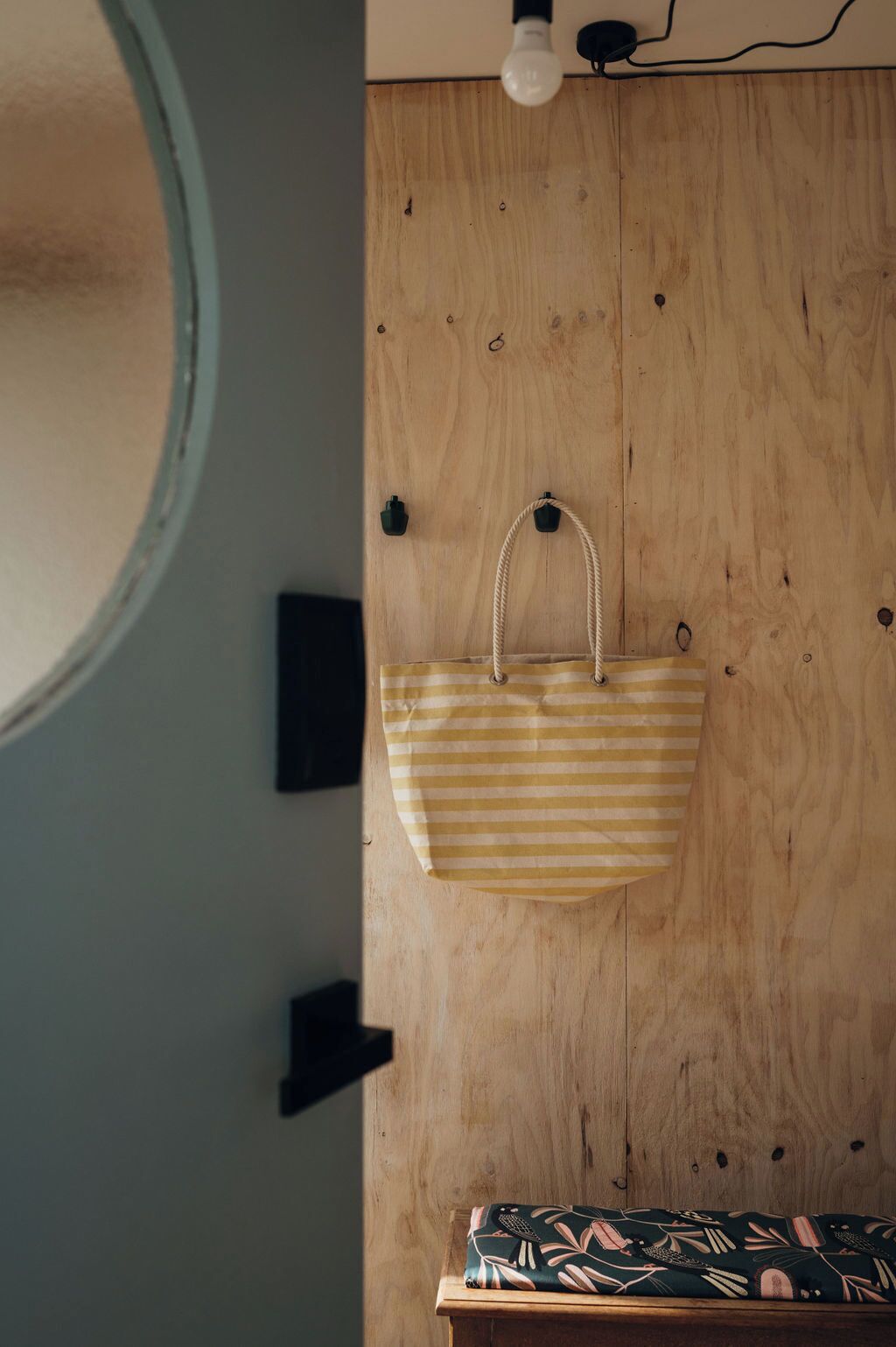 A wooden wall with a hanging striped bag and a light bulb.