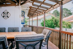 An outdoor covered patio with a wooden table and chairs, a welcome sign, and a view of neighboring houses. - Husky Waters overlooking the moored yachts. (Huskisson)