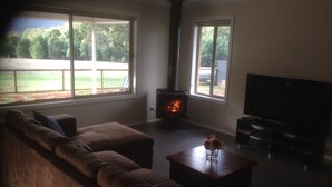A living room with a large window, a fireplace, a sofa, and a TV. - Marysville Views - Peaceful Snow Escape | Spacious 4BR Retreat (Marysville)
