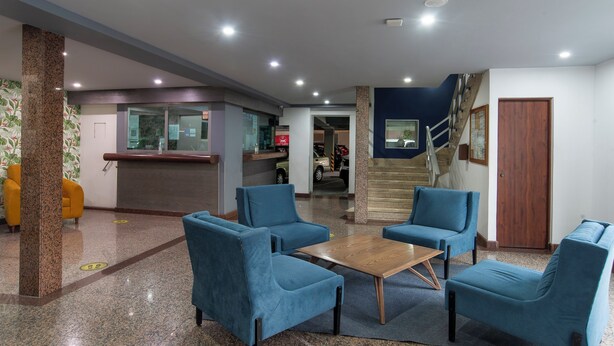 A lobby with a reception desk, blue chairs, a wooden table, and a staircase. - Hotel Menara (Mexico City)