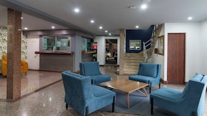 Un hall d’entrée avec un comptoir de réception, des chaises bleues, une table en bois et un escalier.