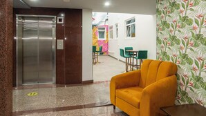 A lobby with a reception desk, a yellow armchair, a staircase, and a wall with a tropical wallpaper. - Hotel Menara (Mexico City)